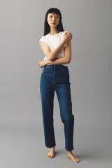 Jean de tiro alto con corte mom slim, confeccionado en denim azul oscuro con leve elasticidad. Presenta diseño de cinco bolsillos, cierre con botón y pierna recta que se estrecha ligeramente hacia el bajo.
