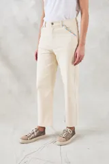 Pantalón jean color crudo, de tiro medio y corte recto, con bolsillos delanteros con bordado de motivos geométricos en tonos celeste y naranja.