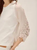 Remera de manga larga color blanco con cuello redondo y detalles fruncidos con lazos en las mangas.