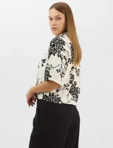 Camisa de corte holgado con estampado botánico en blanco y negro. Presenta cuello camisero, mangas cortas amplias y cierre frontal con botones y vivos a contratono.