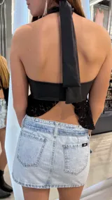 Top negro de cuerina con escote halter cruzado, abertura frontal en el pecho y detalle de volados de encaje en el ruedo.