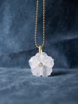 Collar con cadena de eslabones tipo bolita dorada y dije de piedra natural tallada en forma de flor con una pequeña circonia incrustada en el centro.