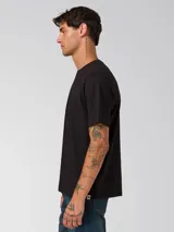 Remera de algodón de corte clásico y cuello redondo, color negro. Presenta un diseño minimalista con un pequeño gráfico bordado en el pecho y un parche de la marca en la manga izquierda.