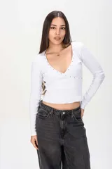 Remera manga larga blanca de tejido acanalado, con profundo escote en V cruzado decorado con tachas metálicas en los bordes.