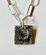 Collar de plata con cadena de eslabones alargados y dije de medalla rectangular con textura rústica, grabado en relieve con forma de estrella y una piedra brillante incrustada en el centro.
