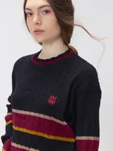 Sweater clásico de punto cable con cuello redondo a la base, mangas largas y fit al cuerpo. De color marrón con franjas horizontales violetas y amarillas, cuenta con el cuello, puños y ruedo acanalados, además de un pequeño logo bordado en el pecho.