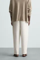 Pantalón blanco de corte relajado (relaxed fit) con pliegues frontales, bolsillos laterales y bolsillos traseros de vivo. Cierre frontal con cremallera y botón.