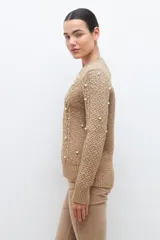 Sweater color beige melange de tejido de punto con diseño de trenzas y detalles de perlas en el frente y las mangas.
