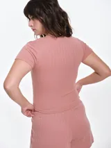 Remera de manga corta entallada en tejido pointelle, con escote redondo y detalle de picot con lazo pequeño en el centro. Diseño ajustado al cuerpo con textura acanalada.