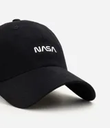 Gorra negra de algodón con visera curva, bordado frontal de la NASA en blanco y aplicación lateral de la bandera de Estados Unidos.