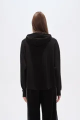 Buzo negro de corte holgado con capucha, manga larga y bolsillo frontal tipo canguro. Presenta un diseño minimalista con una solapa frontal sobre el pecho.