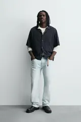 Camisa de algodón negro, de corte relajado (relax fit), con cuello bowling, manga corta y bolsillo plastrón en el pecho. Cierre frontal con botones a presión.