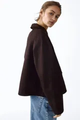 Campera de sarga color marrón oscuro, con cuello camisero de pana, cierre frontal oculto por solapa con botones a presión y bolsillos frontales grandes con solapa.