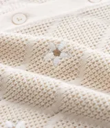 Camisa de manga corta color crema, confeccionada en tejido de punto con diseño de rombos calados y pequeños bordados florales en el centro de cada rombo. Posee cuello cubano y cierre frontal de botones.