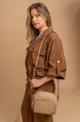 Bandolera de diseño compacto en color beige, confeccionada en material símil cuero con textura granulada. Cuenta con un bolsillo frontal con cierre y correa larga regulable.