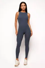 Jumpsuit deportivo de una pieza, color gris oscuro, con cuello alto, sin mangas y diseño ajustado. Presenta un escote profundo en la espalda y costuras estratégicas que realzan la silueta.