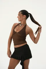 Top halter negro, ajustado al cuerpo, confeccionado en tejido de malla transparente con detalles brillantes o plateados en forma de líneas verticales. Presenta un escote pronunciado en V.