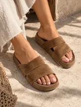 Sandalias planas con base marrón y tiras cruzadas en color beige de textura suave.