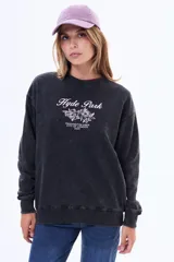 Buzo de felpa con cuello redondo, corte holgado y mangas largas. Presenta un efecto de lavado gastado en color negro y una estampa frontal con texto y diseño floral.