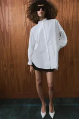 Camisa amplia de algodón con cuello redondo, manga por debajo del codo con puño y bajo asimétrico con aberturas laterales. Presenta cierre frontal con botones ocultos por solapa.