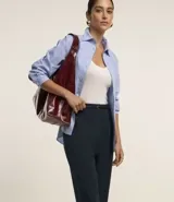 Pantalón de sastrería corte carrot, color beige, con cintura alta, pinzas frontales y cinturón fino incorporado con hebilla metálica.