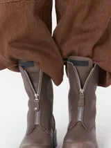 Botas de cuero color marrón de caña alta, con plataforma gruesa de goma y cierre metálico frontal con tirador. Presentan costuras a contratono y detalle de etiqueta de la marca en la lengüeta.