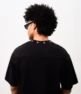 Remera boxy negra de algodón con cuello V decorado con pequeñas estrellas bordadas y un bordado numérico en el centro del pecho.