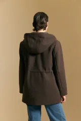 Tapado de paño color marrón oscuro con capucha, cierre frontal oculto con broches, bolsillos aplicados y ajuste interno en la cintura.