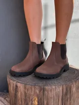 Bota tipo chelsea de cuero marrón con textura granulada, paneles elásticos laterales en color negro y suela track dentada de goma negra.
