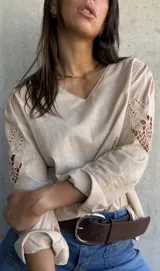 Blusa color beige con escote en V, manga larga y detalles de encaje calado en los hombros.
