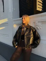 Campera tipo bomber de cuero negro con cuello clásico, cierre frontal metálico y bolsillos frontales con solapa. Presenta un diseño de corte holgado con elástico en la cintura.