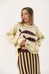 Sweater color manteca de tejido de punto con cuello redondo y ribete marrón. Presenta dos peces marrones tejidos en el frente con detalles bordados a mano.