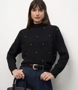 Suéter de punto negro con cuello medio, mangas largas y diseño geométrico sutil. Presenta aplicación de pequeñas perlas o beads distribuidas por el frente de la prenda.