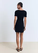 Vestido corto de punto fino en color negro, con escote en pico y detalle de lazo frontal. Presenta mangas cortas y un diseño evasé que aporta movimiento a la prenda.