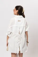 Camisa de lino blanca con silueta amplia y larga, con abertura vertical en la espalda y tiras para atar.