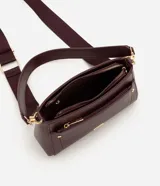 Cartera bandolera de poliuretano color marrón oscuro, con estructura firme y tamaño mediano. Cuenta con un bolsillo frontal con cierre, herrajes metálicos dorados, cierre principal y correa ajustable y desmontable.