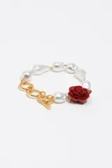 Pulsera de eslabones dorados con cierre de barra en T, decorada con perlas irregulares blancas y un dije central en forma de rosa roja.