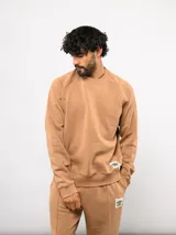Buzo de cuello redondo color tostado, confeccionado en felpa suave, con diseño de mangas raglán y etiqueta con logo de la marca en el frente.