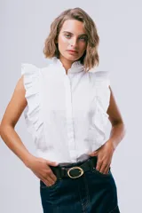 Blusa sin mangas color blanco con cuello alto con volados y detalles de volados en los hombros. Cuenta con cierre frontal de botones.