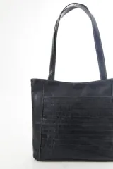 Cartera tipo tote de cuero vacuno negro con doble asa de hombro, panel superior liso y bolsillo exterior frontal con textura símil cocodrilo y costuras visibles en contraste.