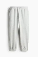 Pantalón de jogging gris claro, de corte relajado, con cintura elástica ajustable con cordón, bolsillos laterales y puños acanalados.