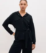 Campera utilitaria deportiva marrón de poliamida, con capucha, cierre frontal de botones, bolsillos con solapa en el pecho y lazo ajustable en la cintura.