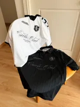 Camiseta de fútbol estilo boxy color blanco, con cuello polo y ribetes negros en las mangas. Presenta detalles estampados y bordados exclusivos en el frente y hombros.