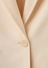 Blazer de diseño recto y estilo sastrero, color beige, confeccionado en mezcla de lyocell y poliéster. Cuenta con cuello en pico con solapas de muesca, manga larga, bolsillos delanteros con solapa y cierre frontal de un botón.
