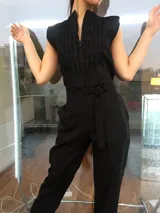 Mono largo de lino color beige, con detalle plisado en el frente, escote en V, sin mangas, lazo en la cintura, cierre invisible delantero y bolsillos laterales.