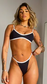 Conjunto de bikini negro con ribetes blancos, compuesto por un corpiño triangular de breteles finos y una tanga de tiro bajo.