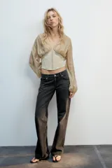 Top beige de manga larga con escote en pico, mangas abullonadas y puños elásticos. Presenta un diseño combinado con tejido fluido en la parte superior y tejido estructurado tipo corsé en la cintura, con cierre frontal de ganchos metálicos.