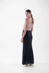 Vestido largo de fiesta con lentejuelas, compuesto por un top verde esmeralda con cuello halter y una falda negra ajustada con abertura lateral.