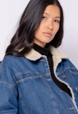 Campera de jean celeste con cuello y forro de corderito color crema, corte cuadrado, cierre frontal con botones metálicos, dos bolsillos de parche en el pecho y elástico en el ruedo.