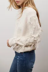 Buzo de punto color beige con cuello redondo, mangas largas con flecos decorativos y diseño de trenzas en el frente.